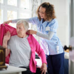 home carer helping senior woman get dressed in her bedroom