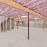 A large-scale basement construction London project in London featuring reinforced concrete walls, steel support columns, and pink fiberglass ceiling insulation in a raw subterranean space.
