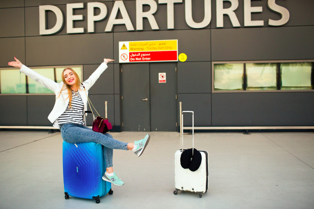 Happy woman raises her hands up sitting on blue suitcase before