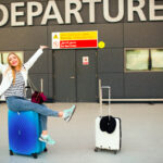 Happy woman raises her hands up sitting on blue suitcase before