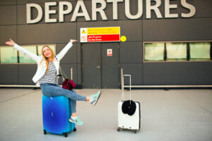 Happy woman raises her hands up sitting on blue suitcase before