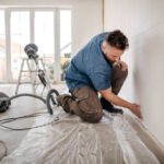 Worker kneels and sands the wall