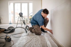 Worker kneels and sands the wall
