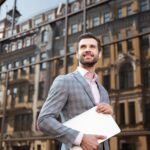 young-serious-man-jacket-holding-laptop-computer-while-standing (1) (1)
