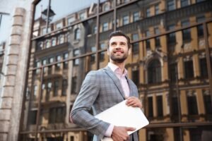 young-serious-man-jacket-holding-laptop-computer-while-standing (1) (1)