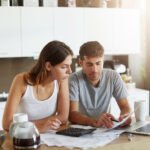 Portrait of serious man and female sitting at kitchen table, dealing with financial issues, holding documents. Family couple calculating their debts while sitting together at kitchen. Business concept